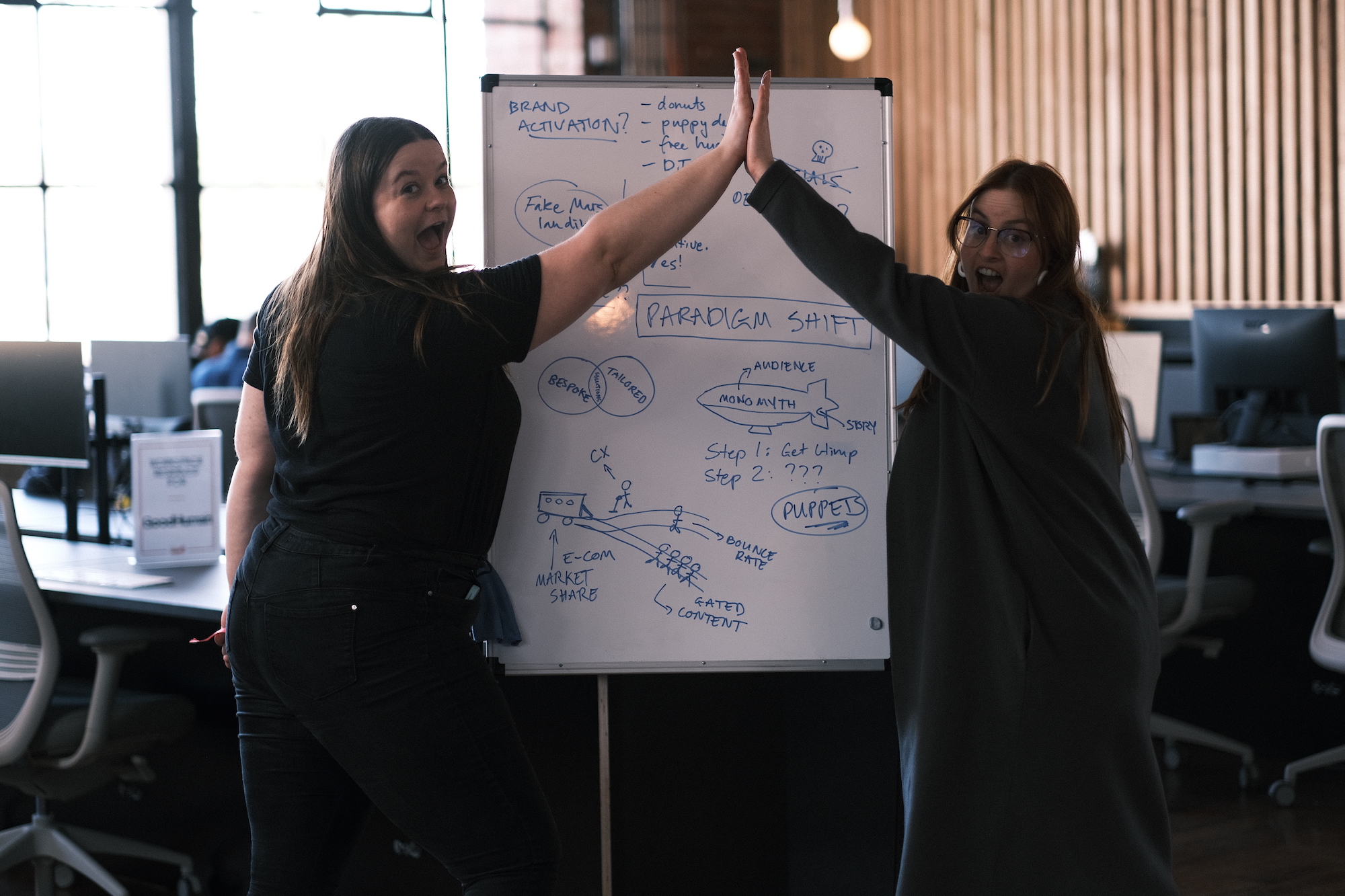Image of Monster & Bear's content agency team high fiving next to a white board